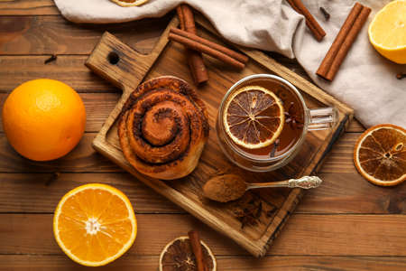 Glass cup of tasty orange tea with cinnamon and roll on wooden backgroundの写真素材