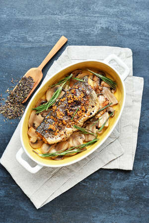 Baking dish with sea bass fish, mushrooms and rosemary branches on gray background