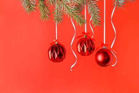 Beautiful Christmas balls hanging on fir branches against red backgroundの写真素材