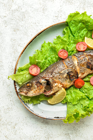 Plate with delicious sea bass fish and vegetables on light background, closeupの写真素材
