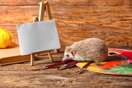 Cute hedgehog with easel and canvas on wooden backgroundの写真素材