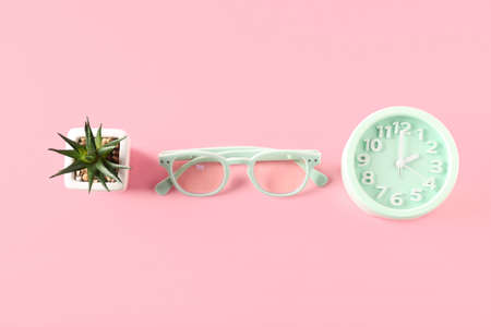 Stylish eyeglasses, alarm clock and houseplant on color backgroundの写真素材