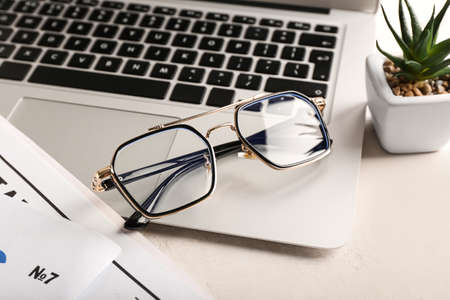 Stylish eyeglasses and laptop on light backgroundの写真素材
