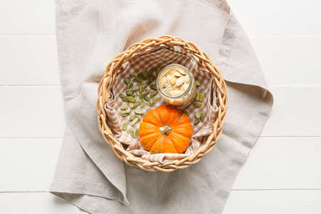 Wicker basket with pumpkin seeds and fresh vegetable on white wooden background