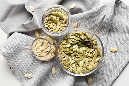 Bowl, jar and jug with pumpkin seeds on white wooden background