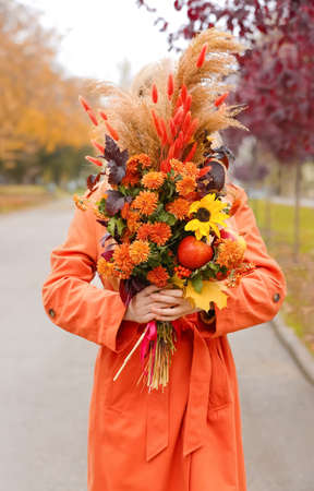 Young fashionable woman holding bouquet in autumn parkの写真素材