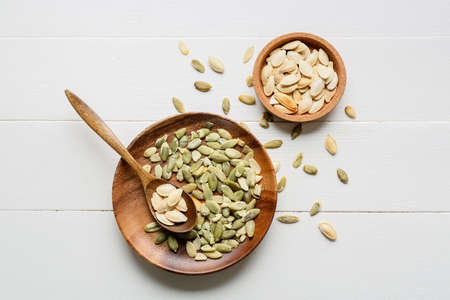 Plate and bowl with pumpkin seeds on white wooden backgroundの写真素材
