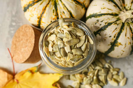 Jar of pumpkin seeds and fresh vegetables on gray background, closeup