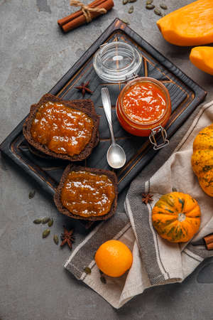 Jar of sweet pumpkin jam with orange and toasts on gray backgroundの写真素材