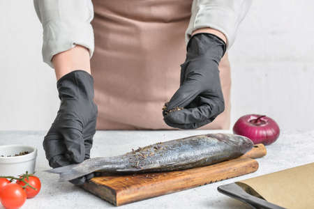 Woman preparing sea bass fish at kitchen tableの写真素材