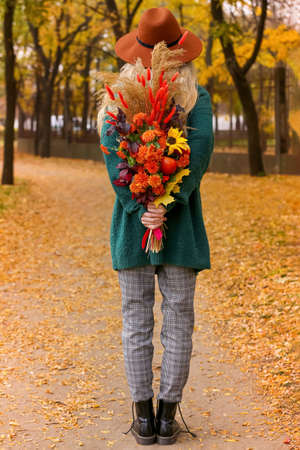 Young woman holding bouquet behind her back in autumn parkの写真素材