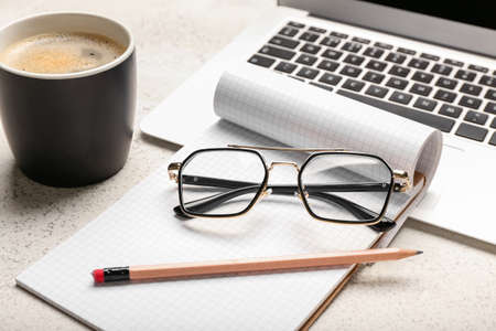 Stylish eyeglasses, notebook, laptop and cup of coffee on light background, closeupの写真素材