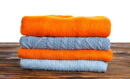 Stack of blue and orange sweaters on wooden table against white background