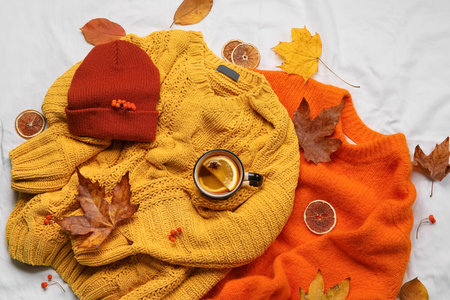 Stylish sweaters, hat, cup of tea and autumn decor on light fabric backgroundの写真素材