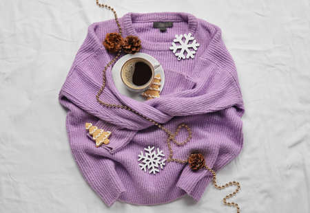 Stylish sweater, cup of coffee, cookies and Christmas decor on light fabric background