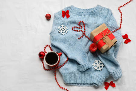 Stylish sweater, cup of coffee, gift box and Christmas decor on light fabric backgroundの写真素材