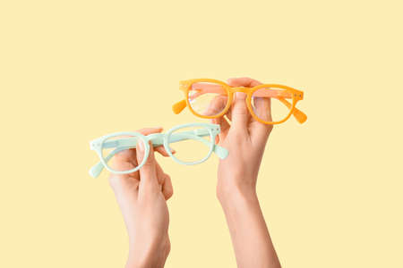 Female hands with different eyeglasses on yellow backgroundの写真素材