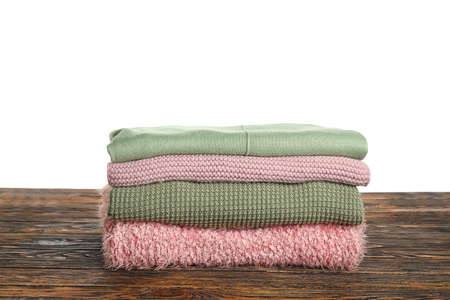 Stack of trendy sweaters on wooden table against white background