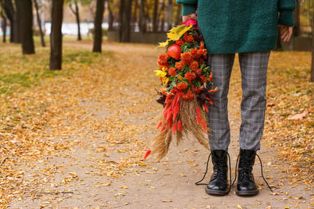 Young woman wearing boots with untied shoelaces and holding bouquet in autumn parkの写真素材