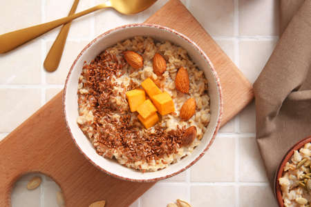 Bowl of tasty oatmeal with pumpkin and almond on tile backgroundの写真素材