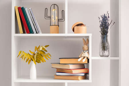 Shelf unit with different books, vases and decor near white wallの写真素材