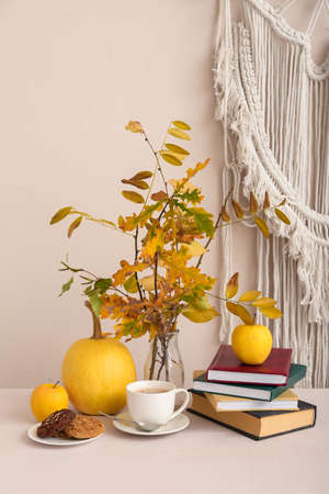 Composition with autumn branches, pumpkin, books, cup of coffee and plate with cookies on table
