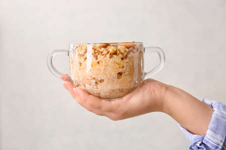 Woman holding pot of tasty oatmeal with pumpkin on light background