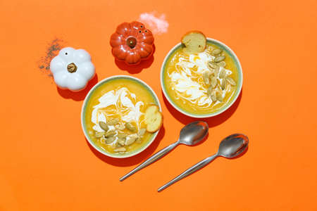 Bowls with delicious pumpkin cream soup and spices on color backgroundの写真素材