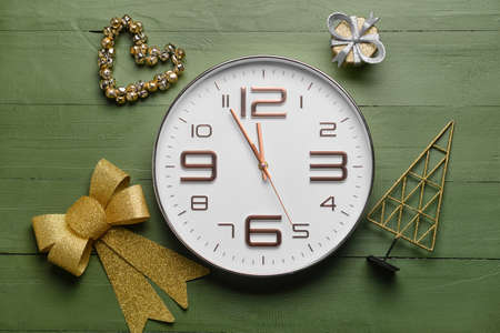 Stylish New Year clock with Christmas decor on green wooden background