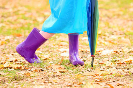 Little girl in stylish rubber boots and with umbrella walking in autumn parkの写真素材