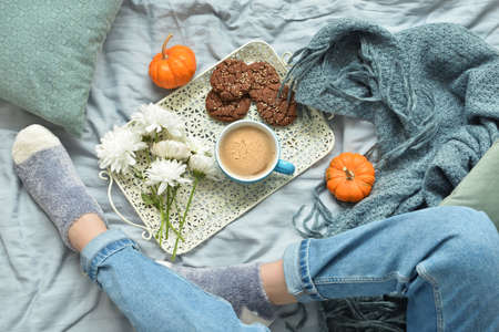 Female legs with beautiful chrysanthemum flowers and cup of tasty pumpkin coffee on bedの写真素材