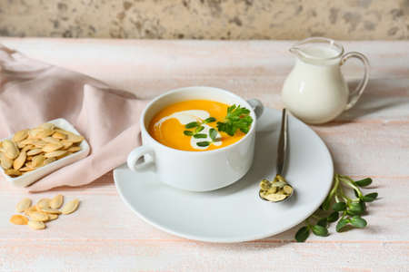 Pot with delicious pumpkin cream soup and seeds on white wooden tableの写真素材