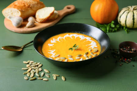 Bowl with delicious pumpkin cream soup and seeds on color wooden backgroundの写真素材