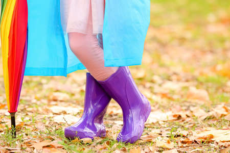 Little girl in stylish rubber boots and with umbrella walking in autumn parkの写真素材