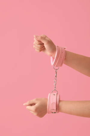 Young woman in handcuffs from sex shop on color backgroundの写真素材