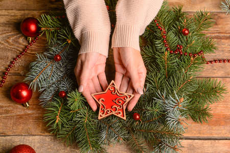 Woman decorating Christmas wreath made of fir branches on wooden backgroundの写真素材