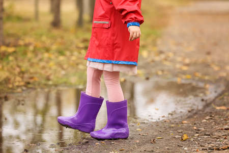Little girl in rubber boots near puddle in autumn parkの写真素材