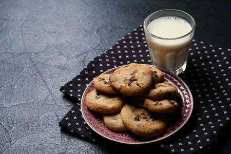Plate with tasty cookies and glass of milk on dark background