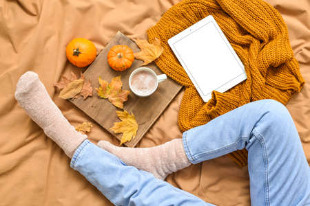 Woman with tablet computer and cup of tasty pumpkin coffee on bedの写真素材
