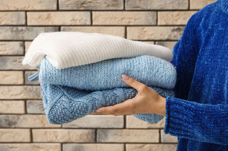 Woman holding stack of warm sweaters on brick wall backgroundの写真素材
