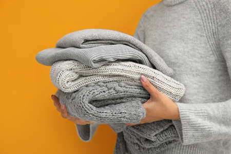 Woman holding stack of stylish sweaters on color backgroundの写真素材