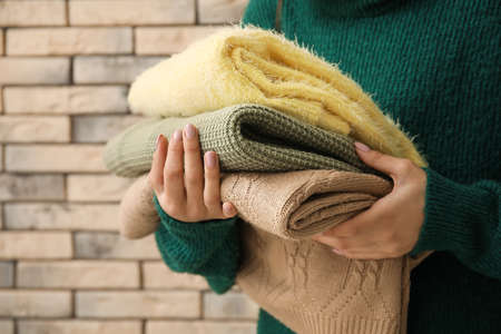 Woman holding stack of soft modern sweaters on brick wall background, closeupの写真素材