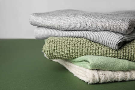 Stack of different sweaters on green table against gray background, closeupの写真素材