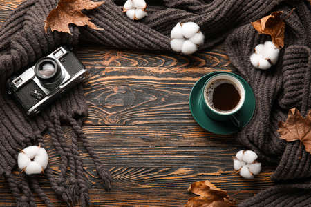 Frame made of knitted scarf, photo camera, cup of coffee and cotton flowers on wooden background
