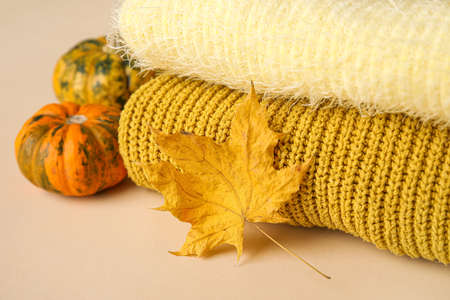Stack of knitted sweaters, dry leaf and pumpkins on table, closeup