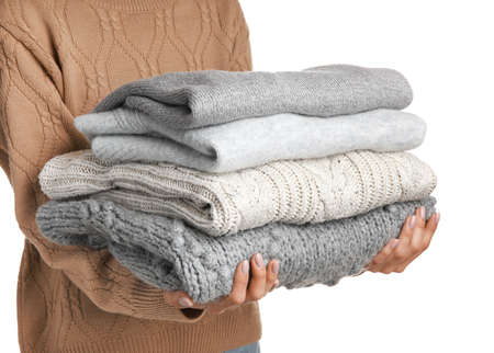 Young woman holding stack of stylish sweaters on white background, closeup