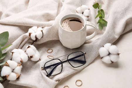 Cup of coffee, eyeglasses, cotton flowers and jewelry on light tableの写真素材