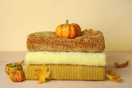 Stylish sweaters, pumpkins and dry leaves on table against color backgroundの写真素材
