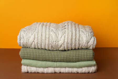 Stack of warm sweaters on table against color backgroundの写真素材