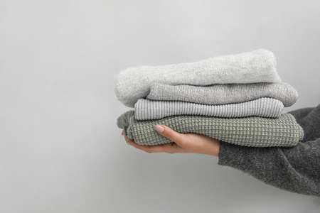 Woman holding stack of warm sweaters on gray backgroundの写真素材